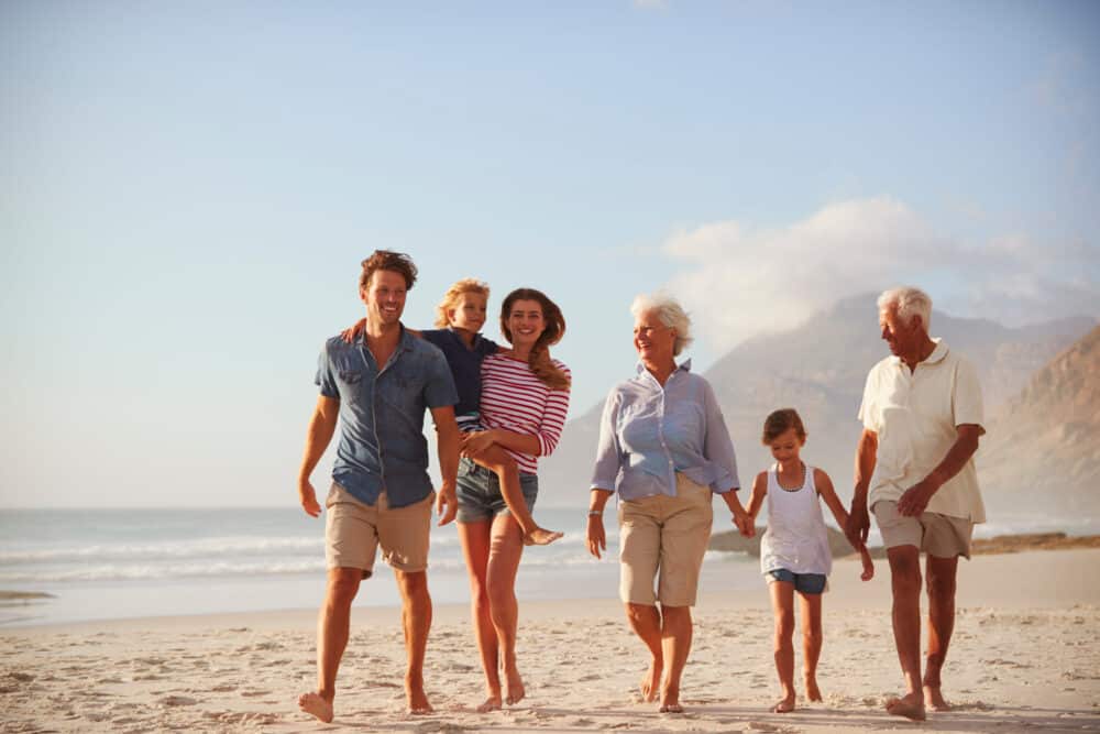 Multi Generation Family On Vacation Walking Along Beach Together