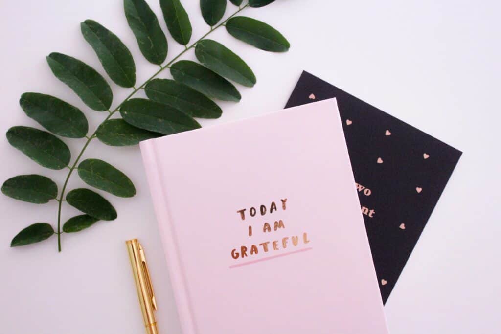 A pink notebook on a desk with the words "I am Grateful" written on the cover.