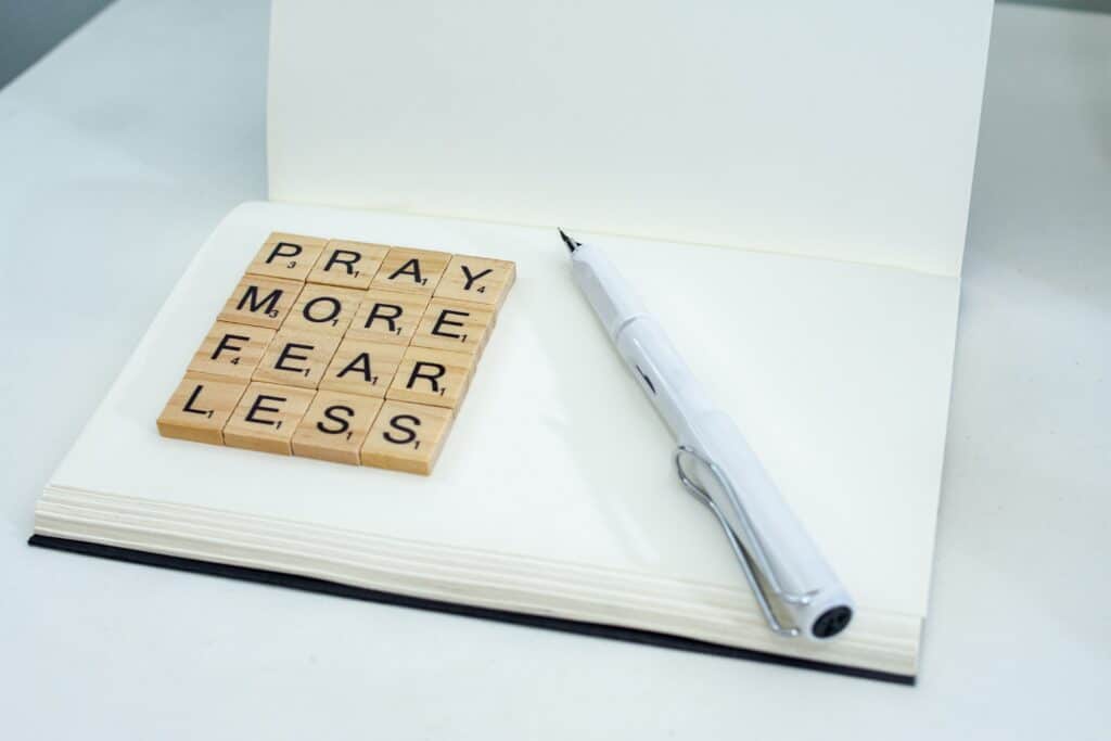 Scrabble tiles spelling out, "Pray more, fear less" on a white notebook.