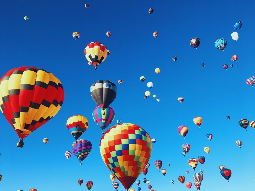 Several bright hot air balloons floating through the blue sky.
