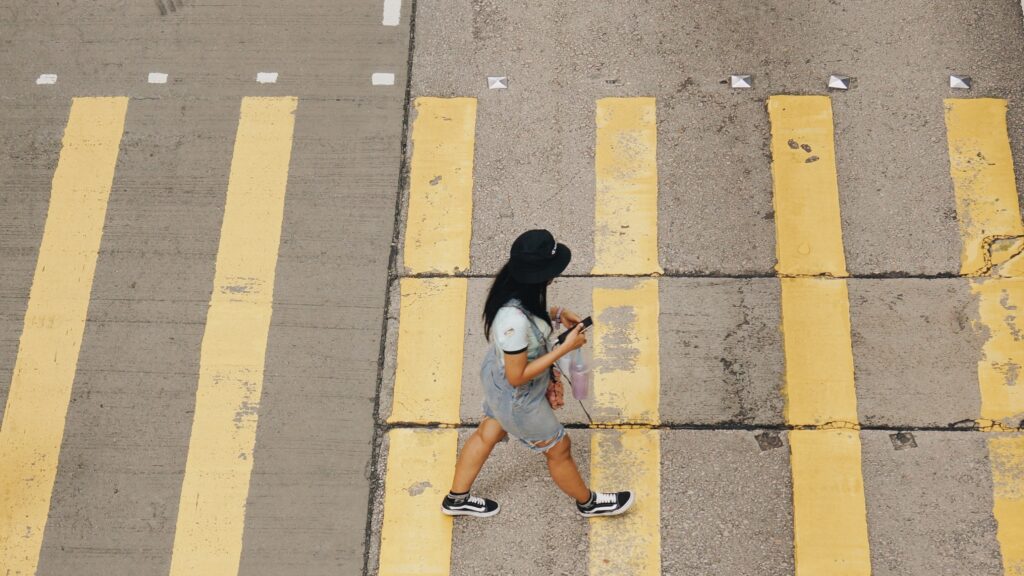 woman crossing street but staring at her phone