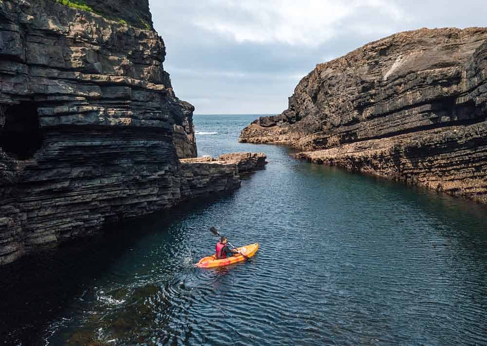 man in kayak going between two cliffs